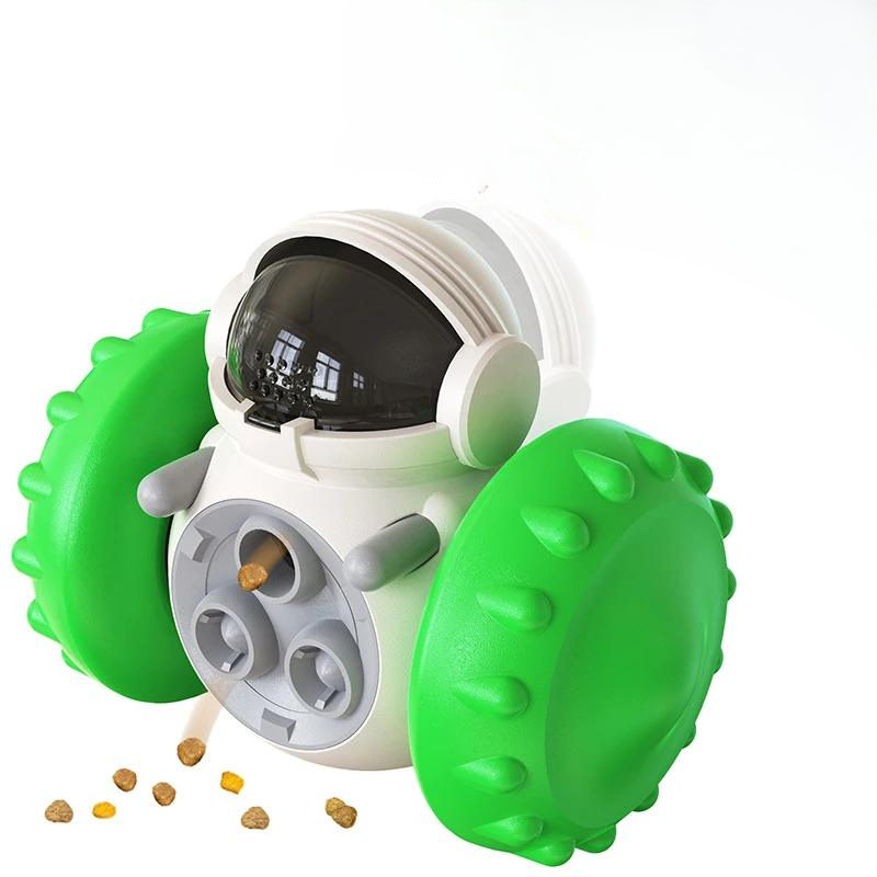 A white robotic device with green, spiky wheels, resembling an astronaut's helmet with its transparent black visor, serves as the Interactive Dog Treat Dispenser & Slow Feeder - Tumbler Toy for Small to Large Dogs. Ejecting small brown pellets from a rotating dispenser on its front, this slow feeder tumbler toy provides both mental stimulation and fun. Background is plain white.