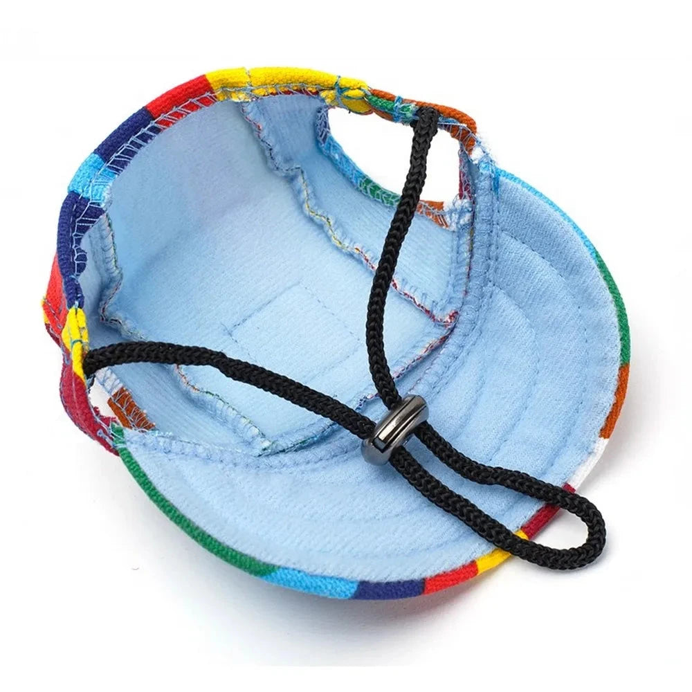 A multicolored pet hat with a light blue interior is shown. This Stylish Canvas Dog Baseball Cap - Perfect for Small Dogs, Outdoor Adventures & Summer Fun has a black adjustable chin strap with a plastic buckle, ensuring an adjustable fit for comfort. The brim is slightly curved and the colorful exterior features a patchwork pattern, offering UV protection.